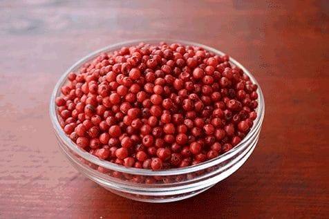 Madagascar Pink Peppercorn — glass bowl on wooden surface
